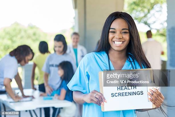 cheerful young african american nurse promotes health fair - film and television screening stock pictures, royalty-free photos & images