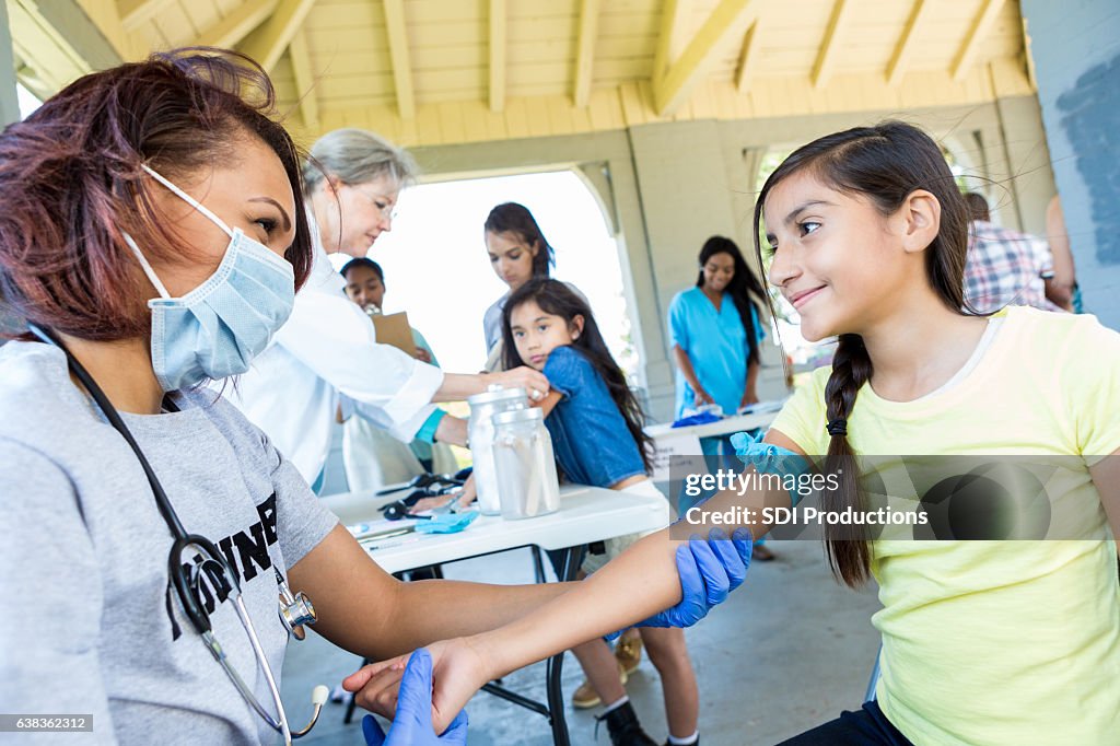 Volunteer doctor prepares to draw blood from a preteen girl