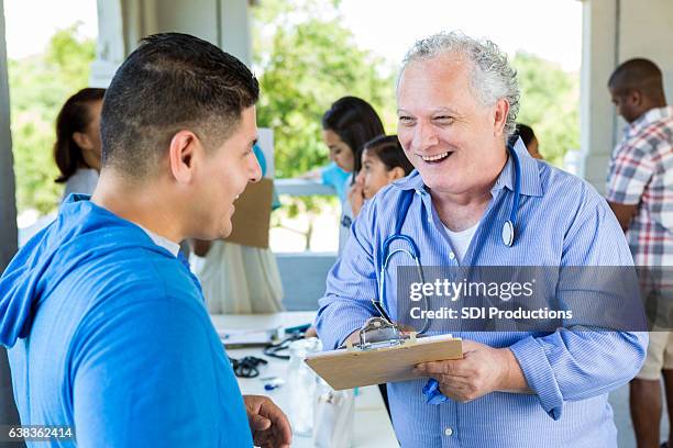 confident senior doctor talks with patient at free outdoor clinic - man stand stockfoto's en -beelden