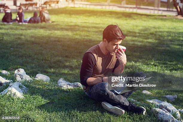 mann studiert am wochenende im stadtpark - mann lässig gras sitzen stock-fotos und bilder