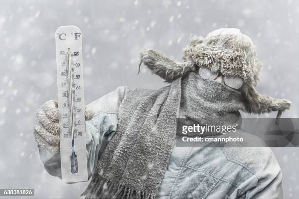 uomo congelato che tiene in mano un termometro mentre nevica - freddo foto e immagini stock