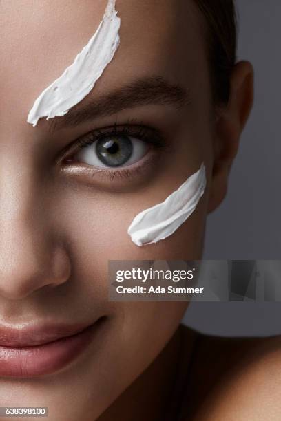 close up portrait of a beautiful woman with cream smear on her cheek - gesichtscreme stockfoto's en -beelden