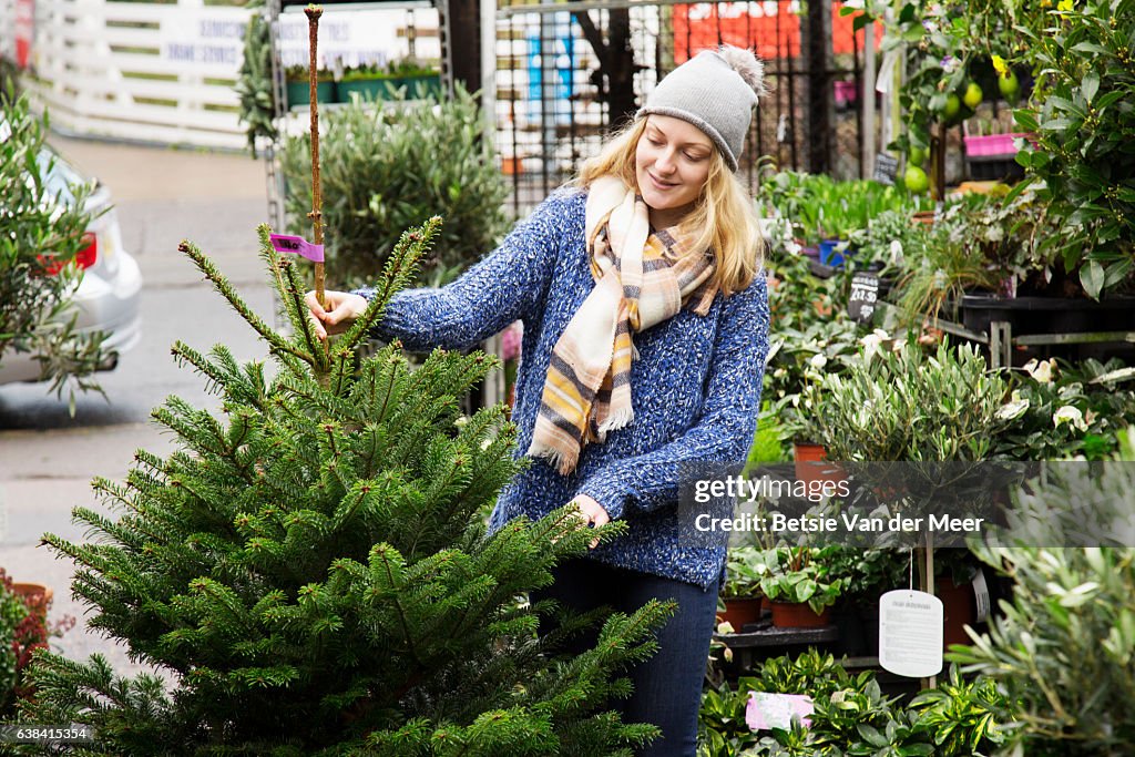 Woman chooses a christmas tree, standing in urban garden center.