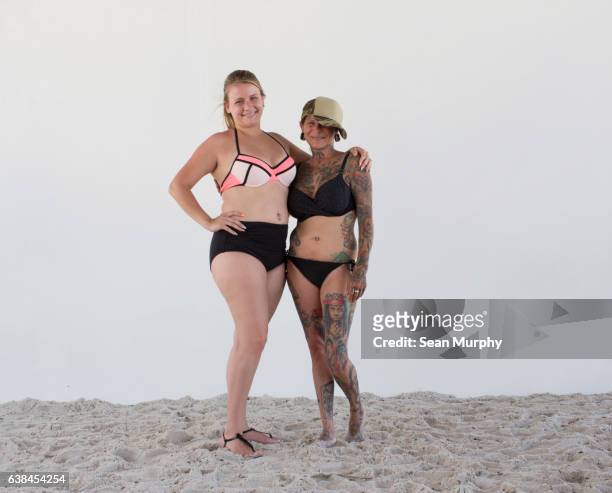 Two woman in bikinis with tattoos on beach with white backdrop