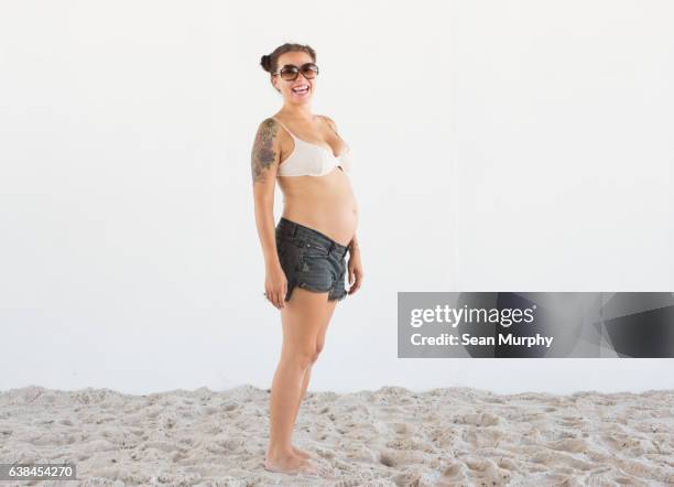 Pregnant woman with tattoos in a bikini at beach with white backdrop