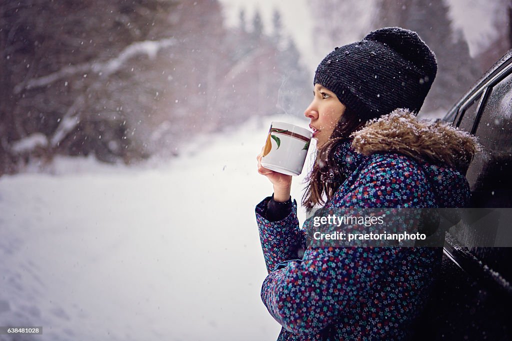 Girl is drinking hot tea in the snowy forest