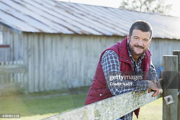 homme à l’extérieur de la grange adossé à une clôture en bois - rancher photos et images de collection