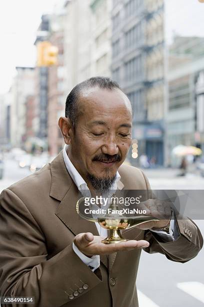 asian mature man rubbing genie lamp in downtown city - djinn stockfoto's en -beelden