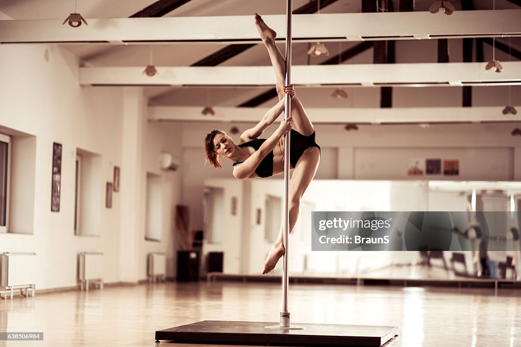 Young female dancer exercising extended frodo on a pole.