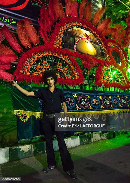 Young Iranian Shiite muslim man mourner pausing proudly in front of an alam on Ashura, the day of the death of Imam Hussein on October 21, 2015 in...