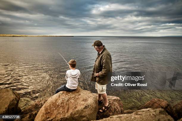 uk, scotland, boy and senior man fishing together - fischen stock-fotos und bilder