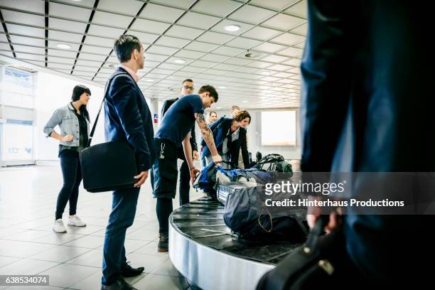 group of travellers waiting for their luggage at baggage claim - travel bag stock pictures, royalty-free photos & images