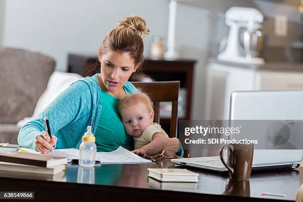 mama arbeitet auf college-auftrag beim kuscheln mit säugling tochter - stereotypical housewife stock-fotos und bilder