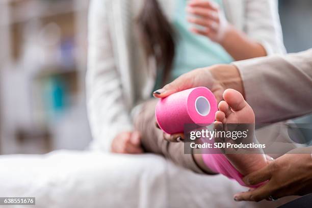 il dottore avvolge la caviglia della ragazza con del nastro sportivo - fasciatura foto e immagini stock