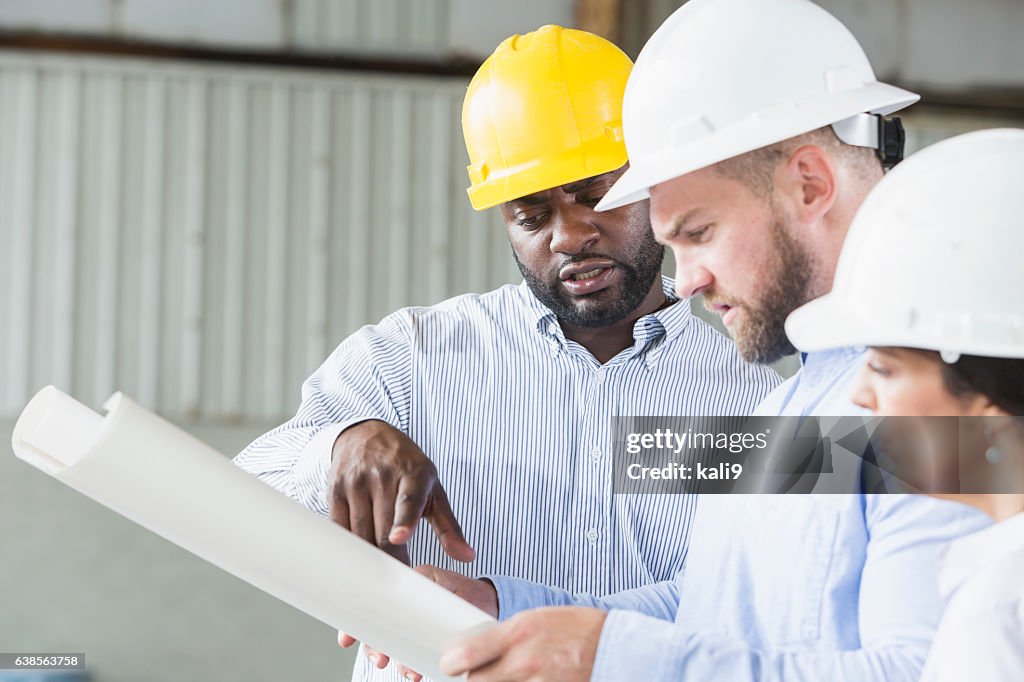 Multi-ethnic workers wearing hardhats looking at plans