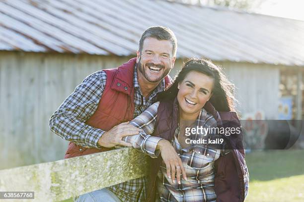 couple leaning on wood fence outside barn - business mature couple portrait stock pictures, royalty-free photos & images