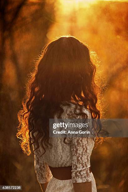 back view of woman with long curly red hair wearing white lace dress, sunset in autumn forest - braunes kleid stock-fotos und bilder