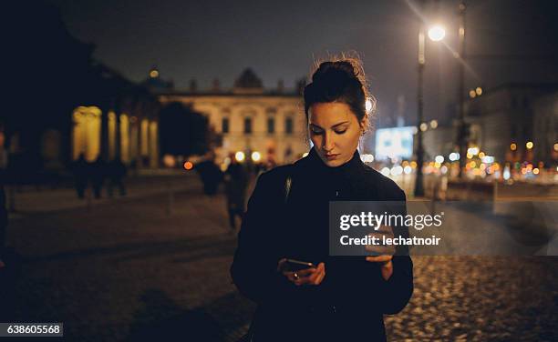 young woman walking in berlin at night checking phone - hair bun scarf woman stock pictures, royalty-free photos & images