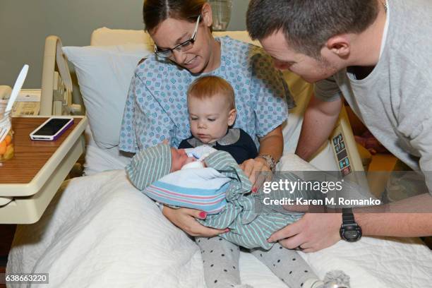 mother holding toddler daughter & newborn son with father looking at baby in hospital - karen novice stock pictures, royalty-free photos & images
