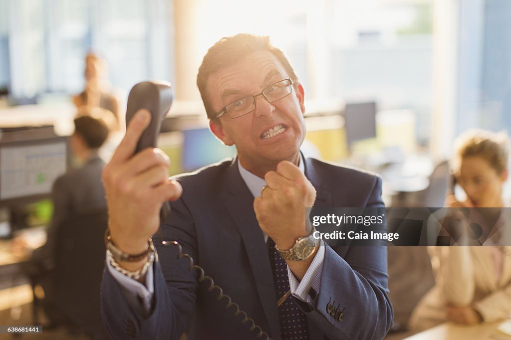 Furious businessman gesturing with fist at telephone in office