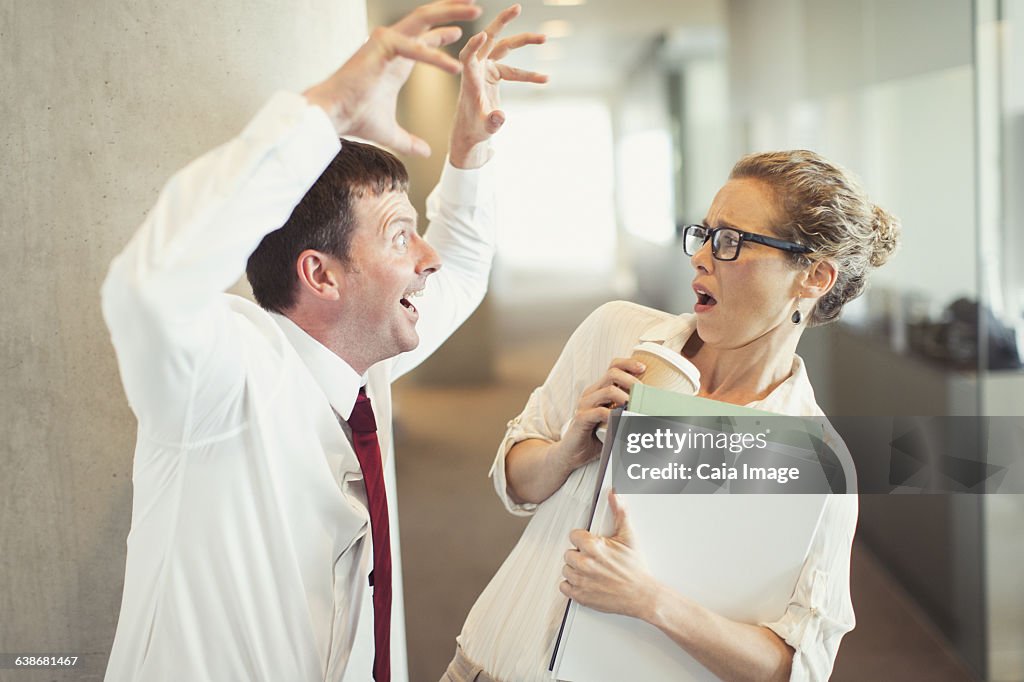 Businessman making snarling gesture at terrified businesswoman