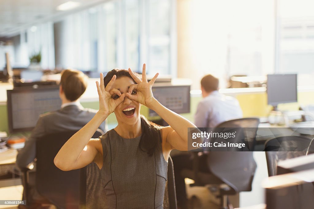 Portrait of playful businesswoman pretending to wear glasses in office