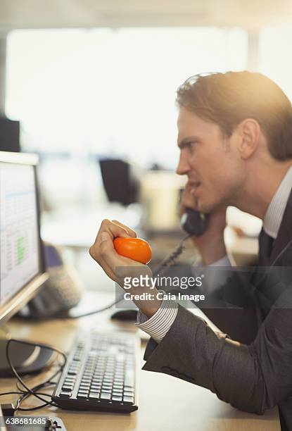 angry businessman squeezing stress ball and talking on telephone at computer in office - stress ball stock pictures, royalty-free photos & images
