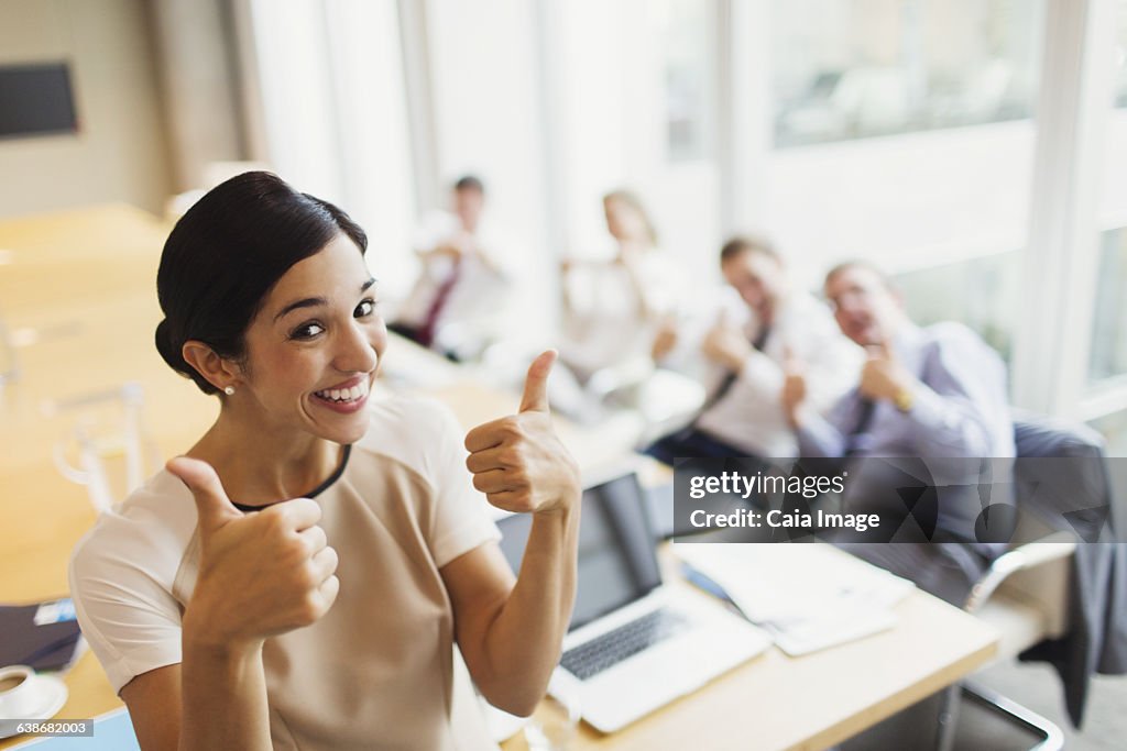 Portrait confident businesswoman and colleagues gesturing thumbs-up in conference room