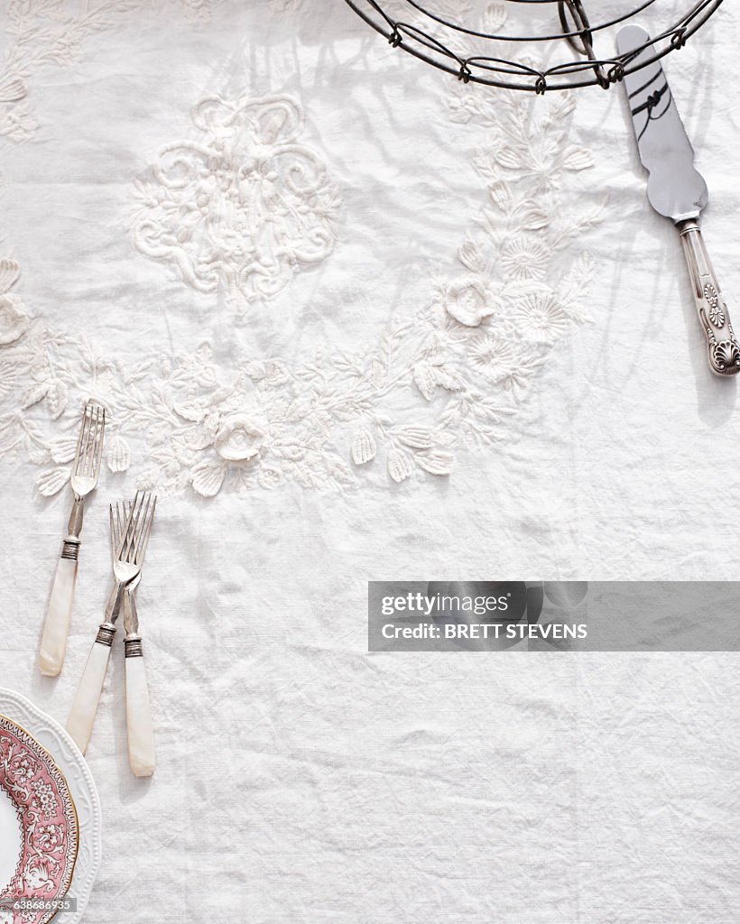 Overhead view of cutlery on white traditional tea tablecloth