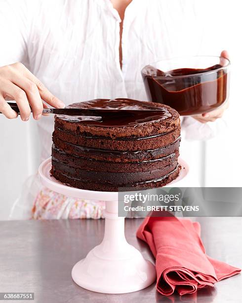 woman icing chocolate layer cake - chocoladeglazuur stockfoto's en -beelden