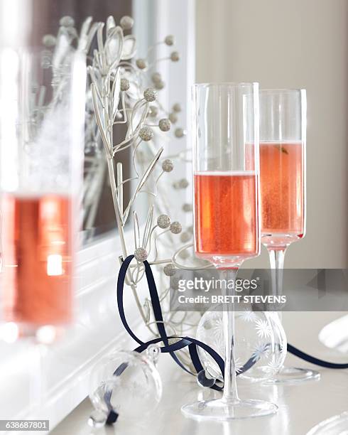 champagne flutes of pink champagne on mantelpiece with christmas decorations - prosecco stock-fotos und bilder
