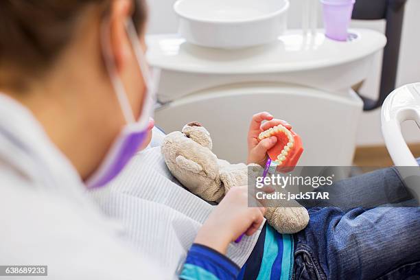 cropped view of boy in dentist chair holding teddy bear brushing dentures - prevención de enfermedades fotografías e imágenes de stock