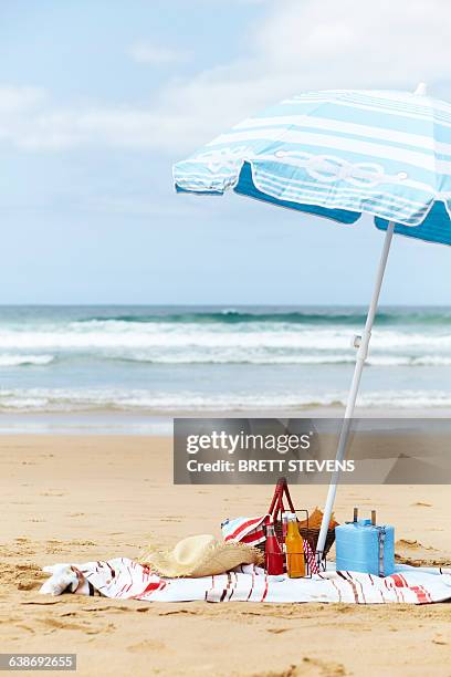 sunhat, cool box and picnic basket on beach towel underneath parasol on beach - beach towel stock pictures, royalty-free photos & images