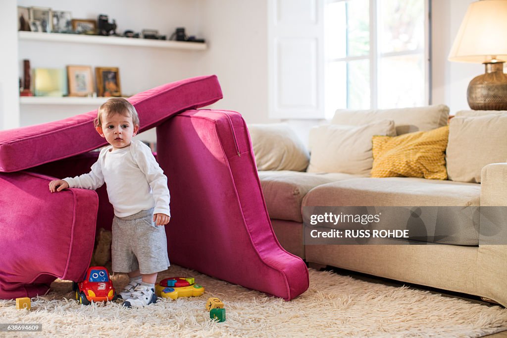 Baby boy playing in fort made from sofa cushions