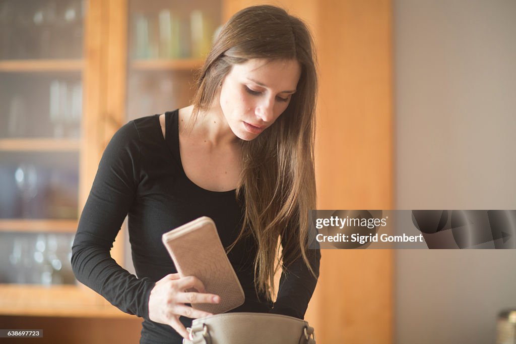 Young woman at home, looking through handbag