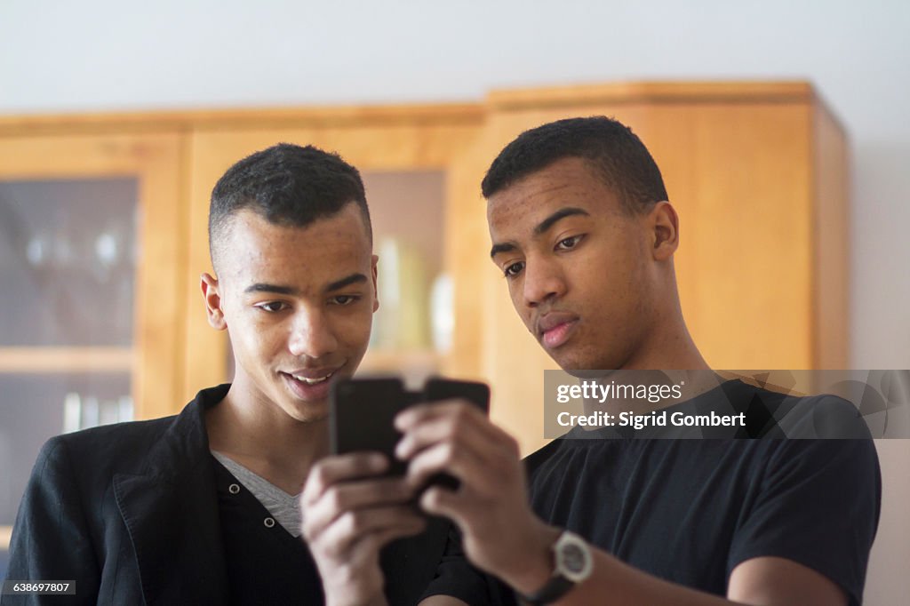 Twin brothers at home, looking at smartphone
