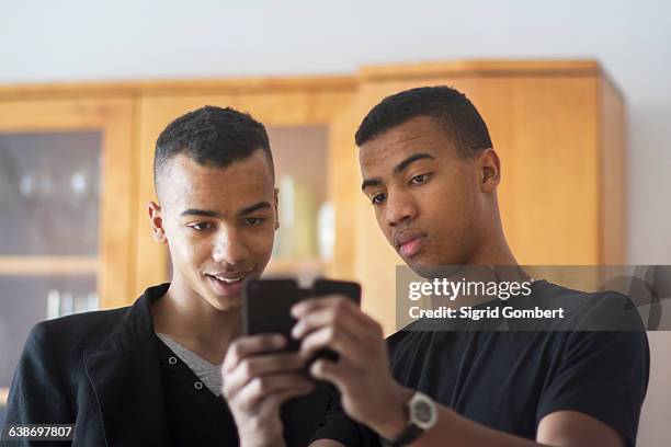 twin brothers at home, looking at smartphone - twin males stock pictures, royalty-free photos & images