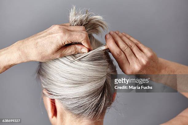 rear view of woman styling gray hair into bun - hochfrisur stock-fotos und bilder