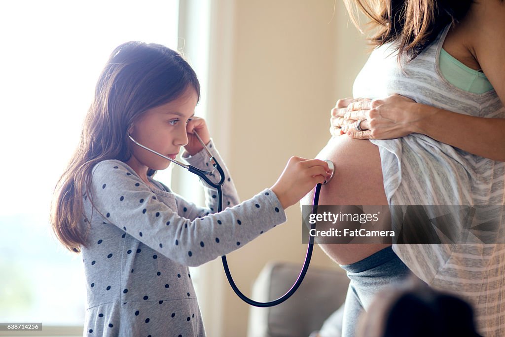 Young girl uses stethescope to listen to pregnant mothers belly