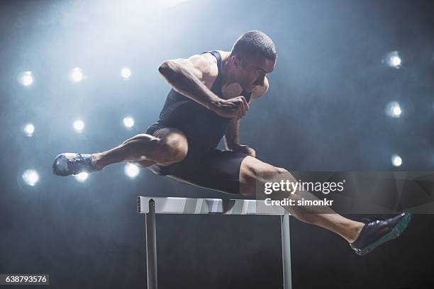 athlete jumping over hurdle - hordelopen atletiekonderdeel stockfoto's en -beelden