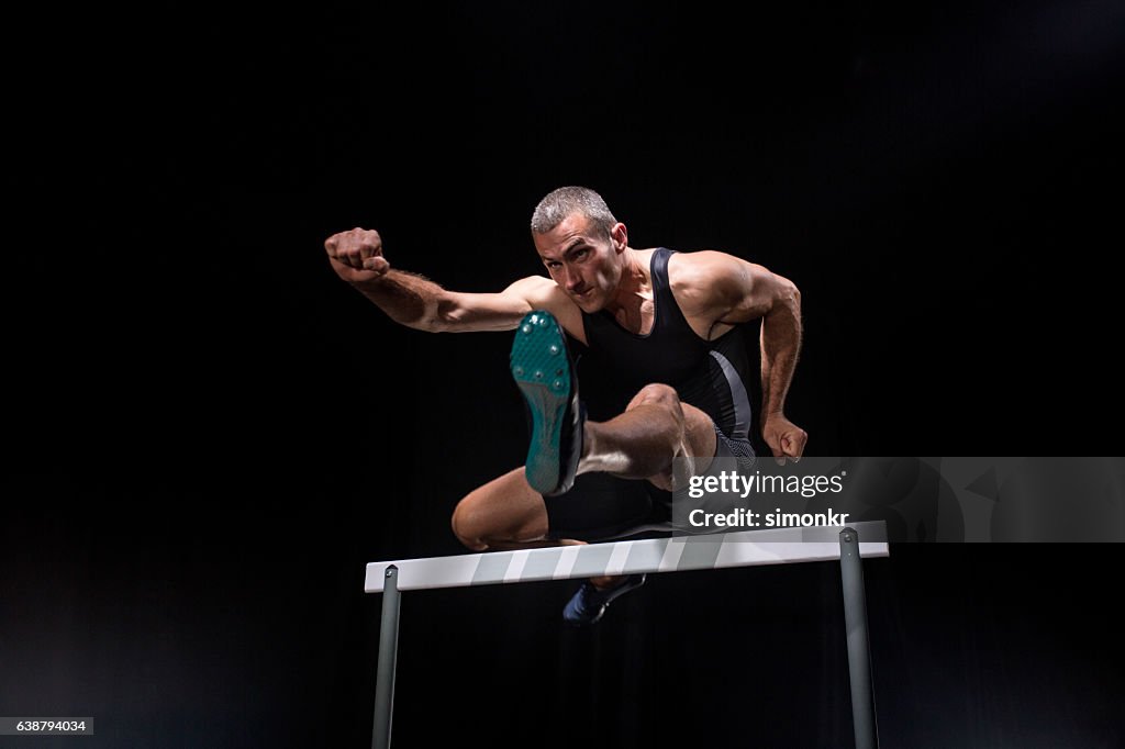 Athlete jumping over hurdle