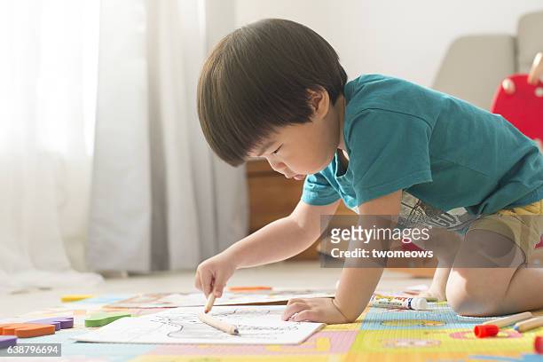 asian young child colouring on floor. - kid holding crayons stockfoto's en -beelden