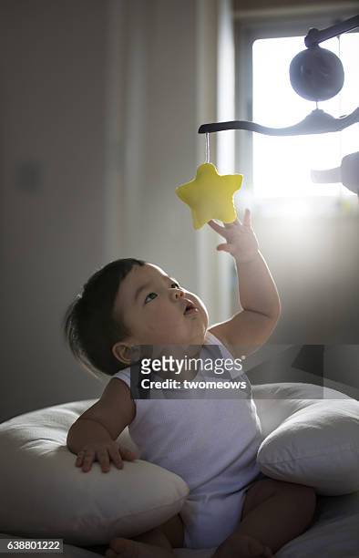 asian toddler boy reaching out to catch a rotating toy star. - baby reaching stock pictures, royalty-free photos & images