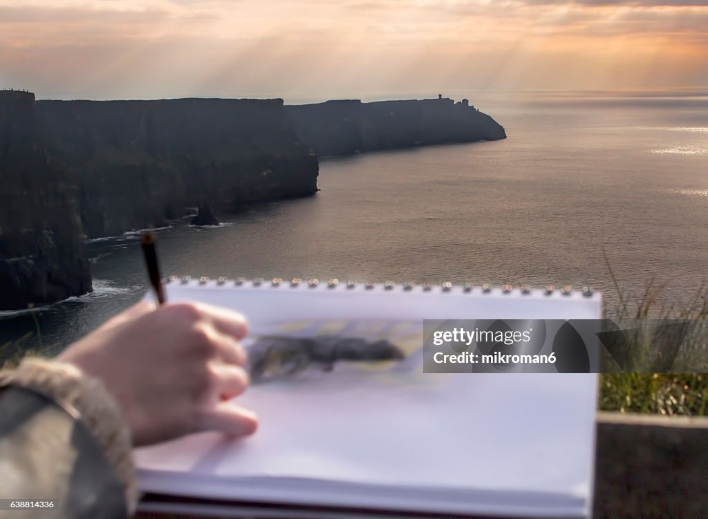 Young woman drawing scenic View Of Cliffs Of Moher, Ireland