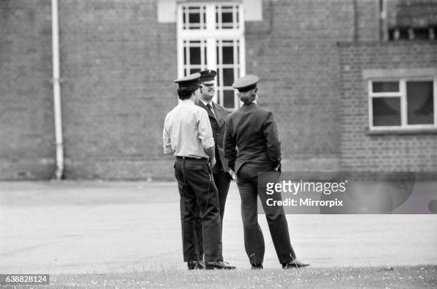 Policemen watch as Michael Peterson stages a protest on the roof of Broadmoor Hospital. 20th June 1983.