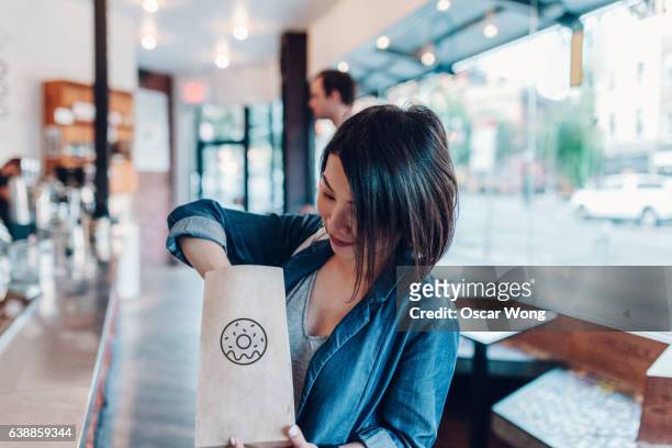 young woman eating donut in a cafe - eating donuts stockfoto's en -beelden