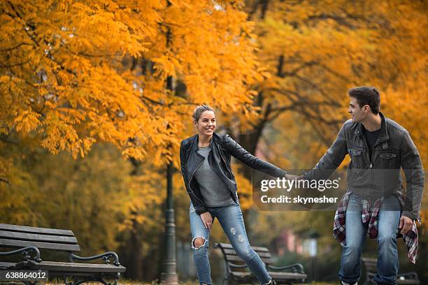 young couple holding hands and roller skating through autumn park. - inline skating man park stock pictures, royalty-free photos & images