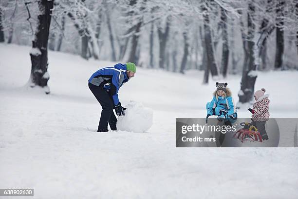 family making snowman outdoors - schneemann bauen stock-fotos und bilder