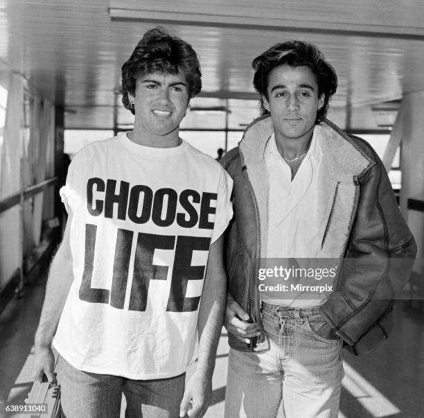Andrew Ridgeley and George Michael of the pop group Wham!, arriving at London airport. George Michael is wearing a 'Choose Life' t-shirt and holding...