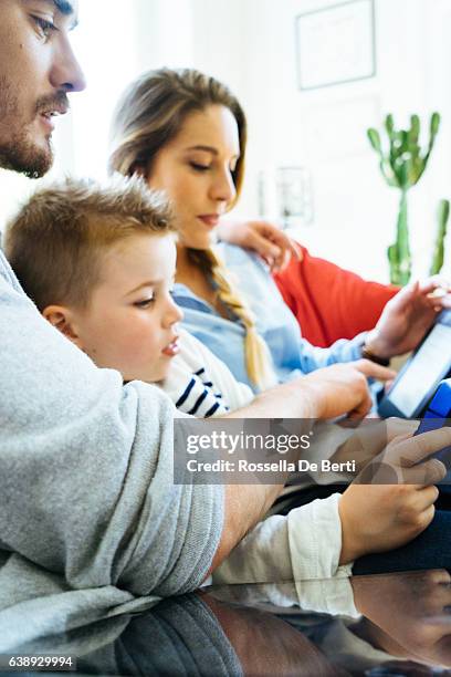 allegra giovane famiglia che usa la tecnologia insieme nel soggiorno - famiglia multimediale foto e immagini stock